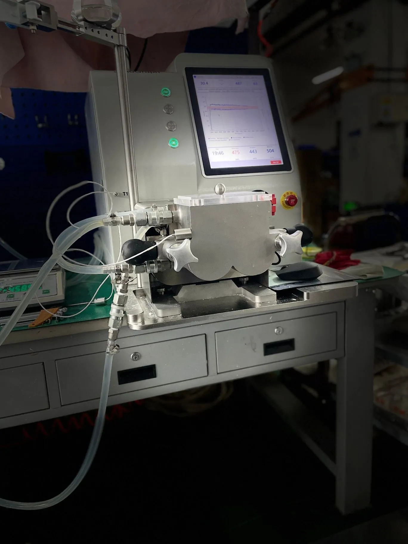 Closer front-left view of the JenoGraph machine, highlighting the sample area, controls, and connected tubing.