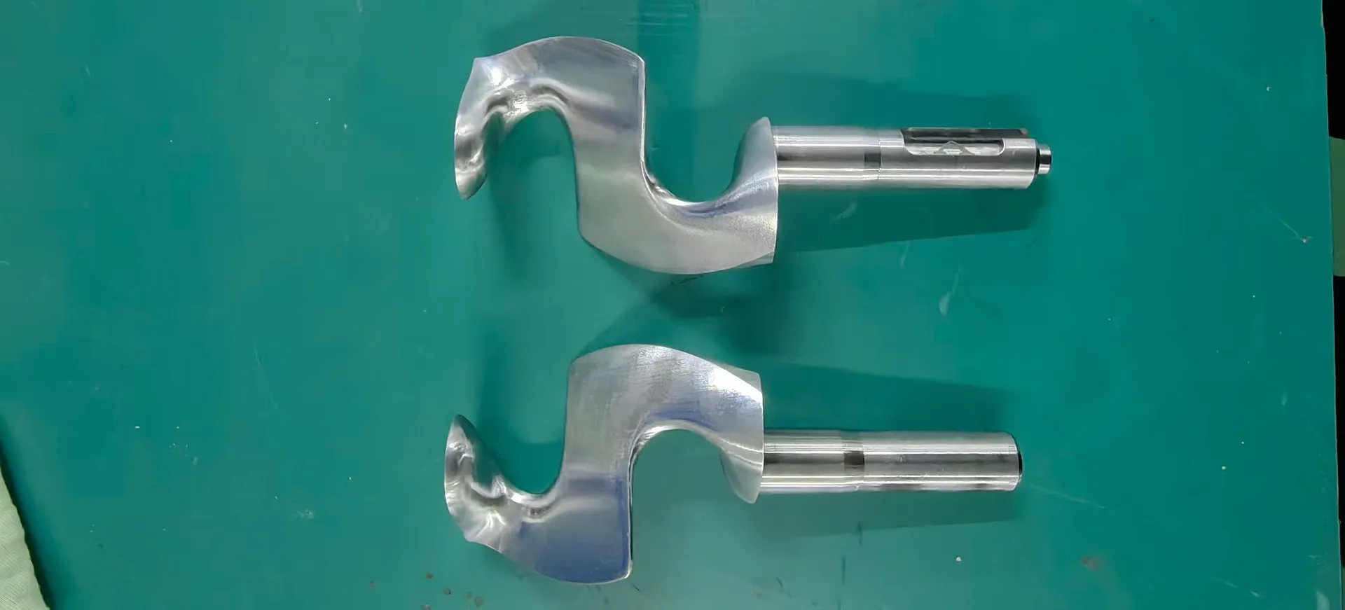 Two JenoGraph blades with cylindrical metal shafts lying on a green work surface.