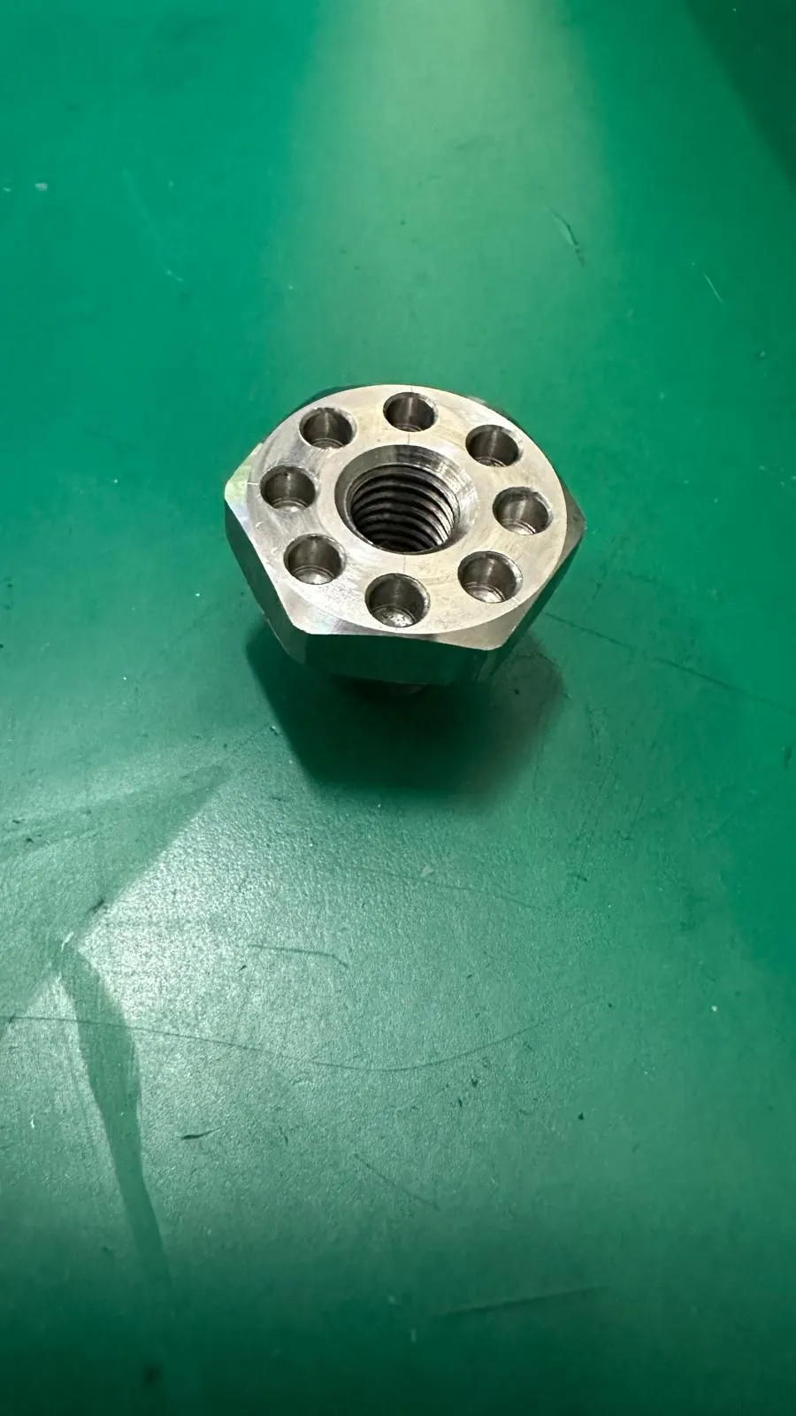 A locking nut with a threaded center and several surrounding openings on a green work surface.