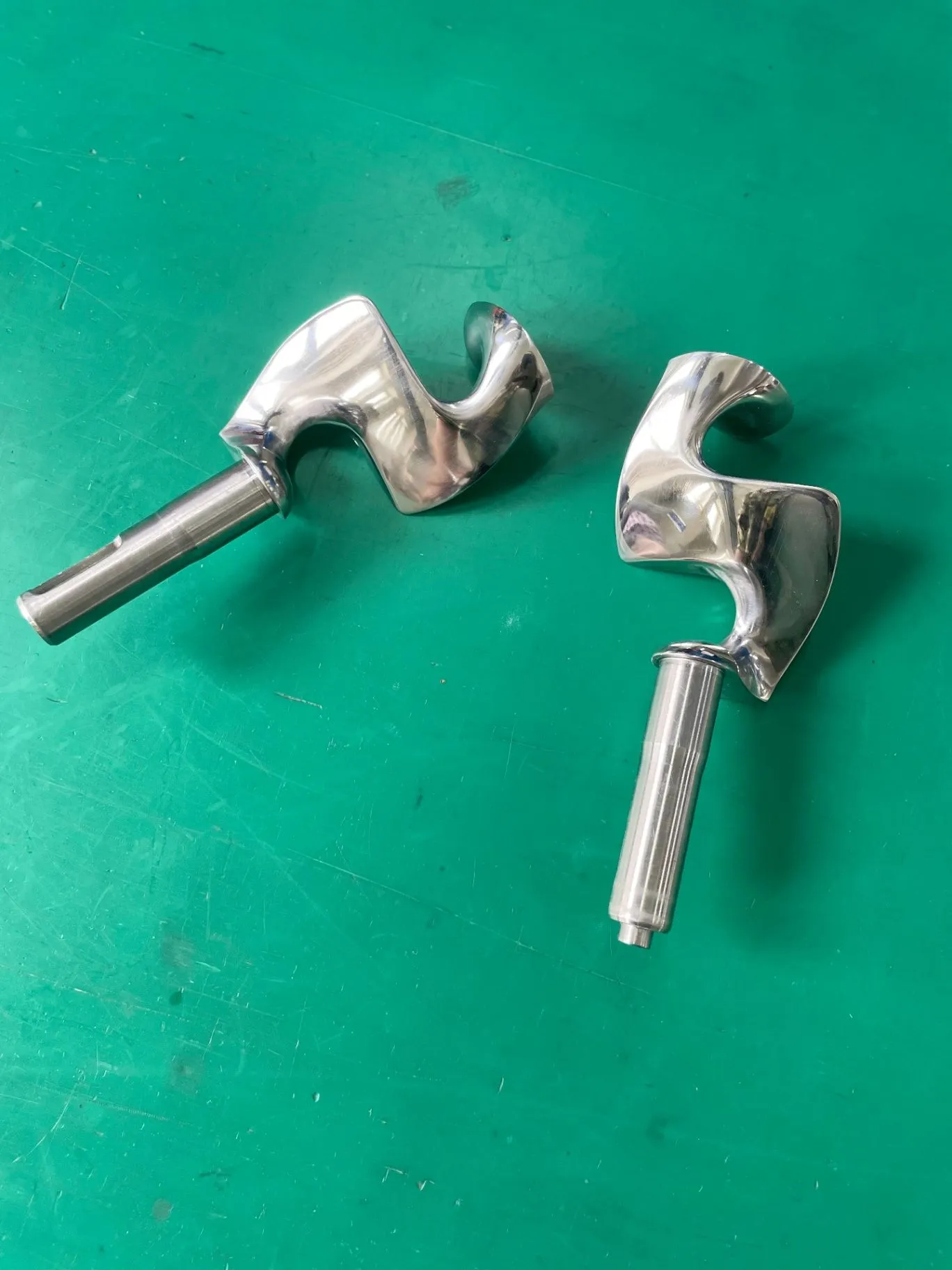 Two polished stainless-steel mixing tools lying on a green work surface.